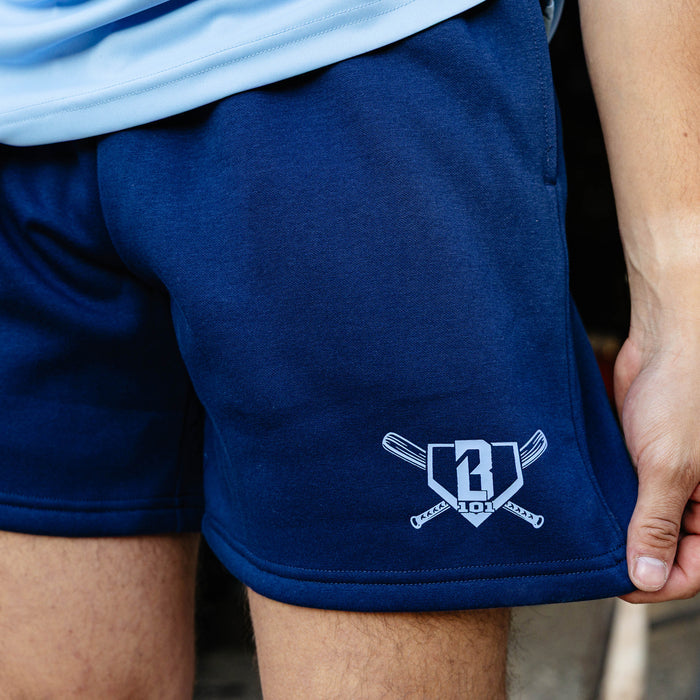 Detail shot of the navy Heritage Diamond Sweatshort highlighting the white BL101 crossed bats home plate graphic on the lower left leg with the shorts fabric texture visible.