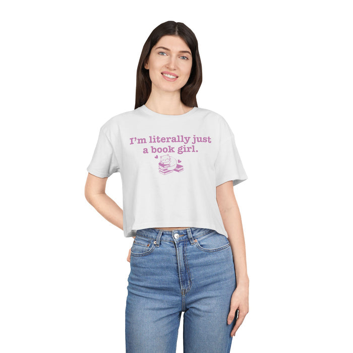 thtgrlreads apparel featuring a white cropped t-shirt from Printify with vintage wash, part of the Tees collection, printed with soft pink text reading "I'm literally just a book girl" above a stack of books graphic.