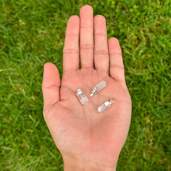 Three small clear crystal point pendants resting on an open palm, photographed outdoors against a blurred green grass background.