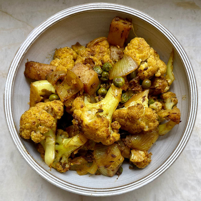Bowl of roasted vegetables including cauliflower and potatoes on a marble surface