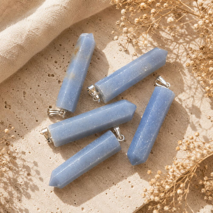 Angelite point pendants displayed on a natural stone surface with soft linen and dried botanicals.
