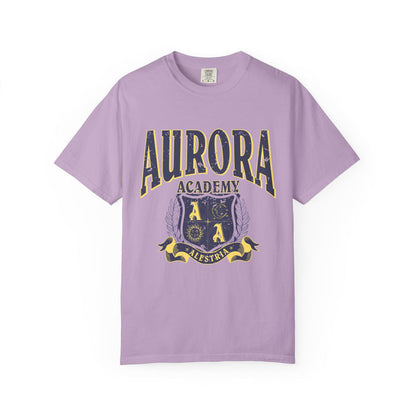 A vintage wash lilac Comfort Colors graphic tee from thtgrlreads featuring a distressed print of Aurora Academy with a crest emblem, part of the Ruthless Boys of the Zodiac and Back to School collections.