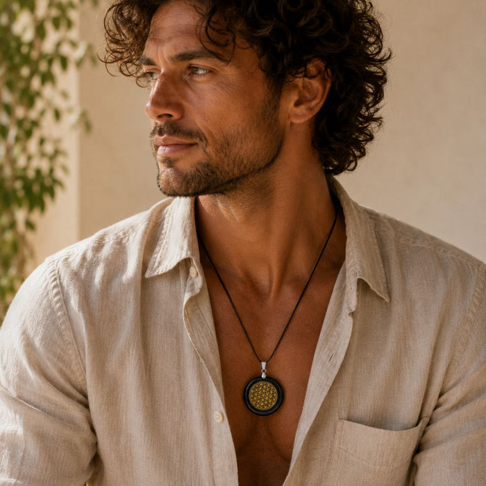 A man wearing a black cord necklace with a round pendant featuring a gold geometric pattern on a dark background, styled with a light beige linen shirt.