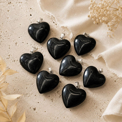 Black heart-shaped pendants on a beige fabric background with dried flowers.