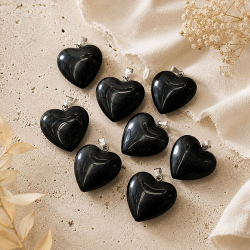 Black heart-shaped pendants on a beige fabric background with dried flowers.