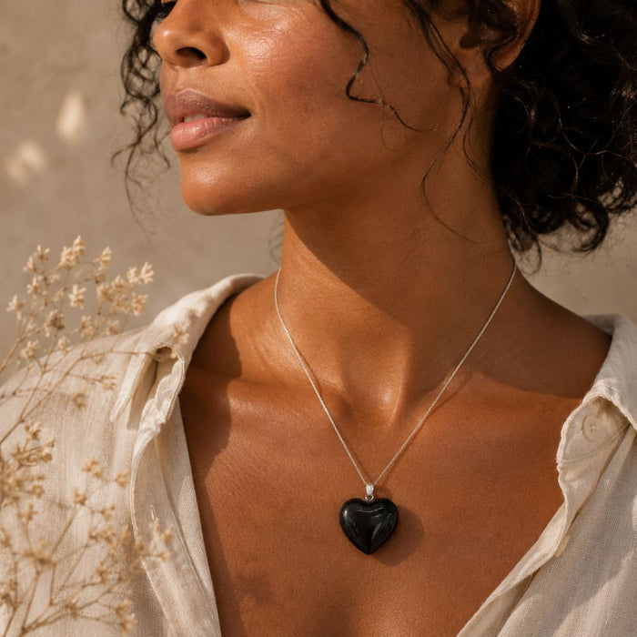 Woman wearing a necklace with a heart-shaped pendant, surrounded by dried flowers.
