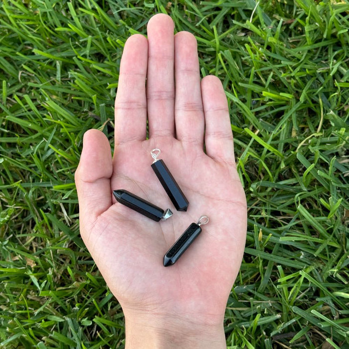 Black Obsidian crystal point pendants displayed in the palm of a hand for size reference.