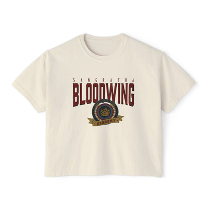 A cream-colored unisex Comfort Colors cropped t-shirt featuring a vintage wash and bold Bloodwing Academy graphic text with a circular emblem in maroon and gold, thtgrlreads.
