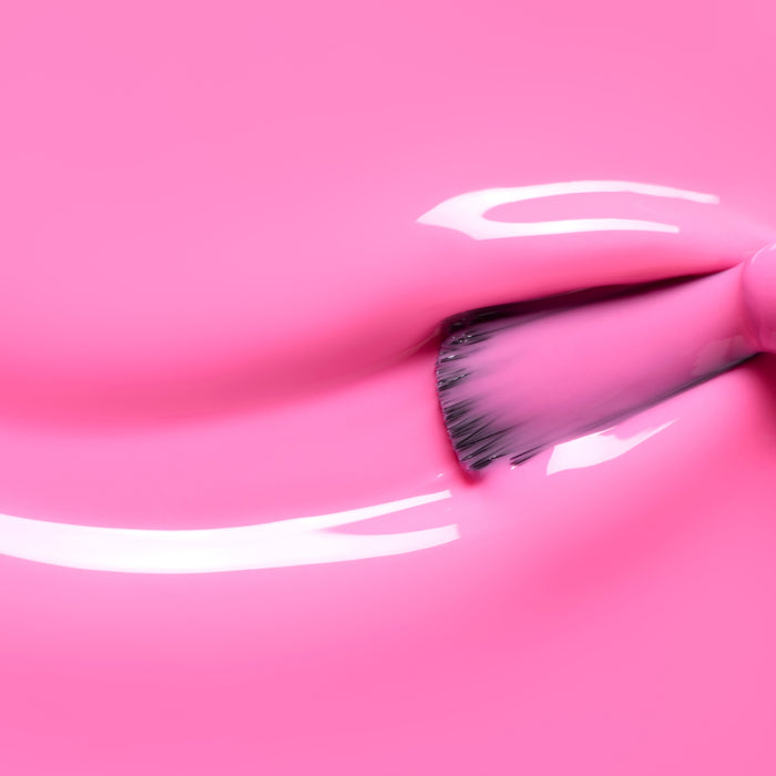 A close-up of a brush applying Manucurist’s Bloom gel polish in neon pink, creating shiny, reflective streaks and a magnetic intensity on a smooth surface.