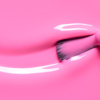 A close-up of a brush applying Manucurist’s Bloom gel polish in neon pink, creating shiny, reflective streaks and a magnetic intensity on a smooth surface.