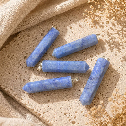 Blue Quartz point pendants displayed on a natural stone surface with soft linen and dried botanicals.