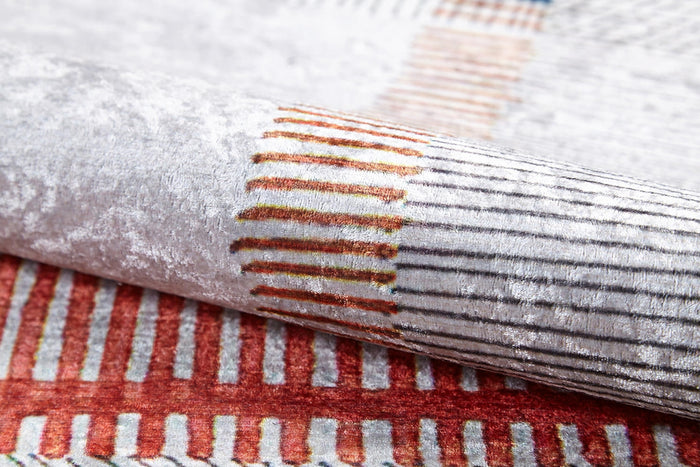 A close-up of the Bohemian Nightscape - Washable Rug (JR1701) shows its soft, textured fabric and modern geometric pattern in red, orange, and beige on a white-gray background—durable and stylish for high-traffic areas.