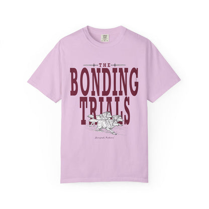 Comfort Colors graphic tee from thtgrlreads featuring vintage wash fabric in lavender with bold "The Bonding Trials" text and a detailed black and white wolf illustration, part of the Wolves of Ruin collection.
