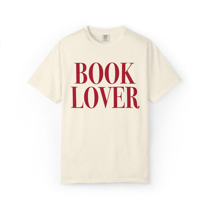Thtgrlreads comfort colors graphic tee from the Tees collection featuring a vintage-wash cream base with bold red serif text reading "BOOK LOVER" on the front.