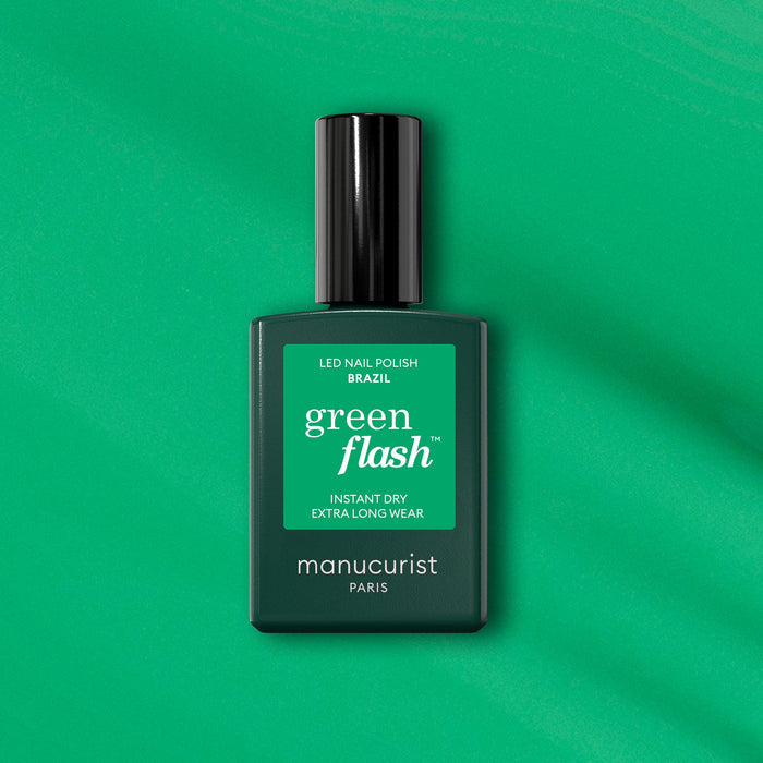 A bottle of Manucurist Brazil Green Flash LED polish sits on a green background, featuring instant dry and extra long wear for vibrant electric green nails inspired by Copacabana Beach.