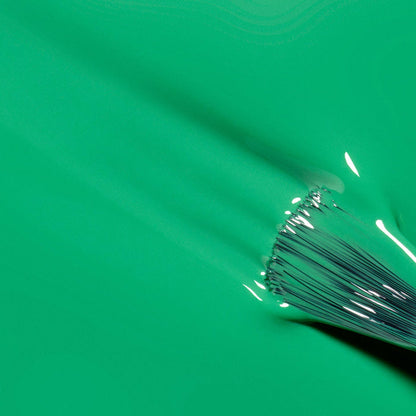 A close-up of a paintbrush smoothly applying Manucurist's Brazil electric green nail polish, showing glossy, wet texture and distinct brush bristles.