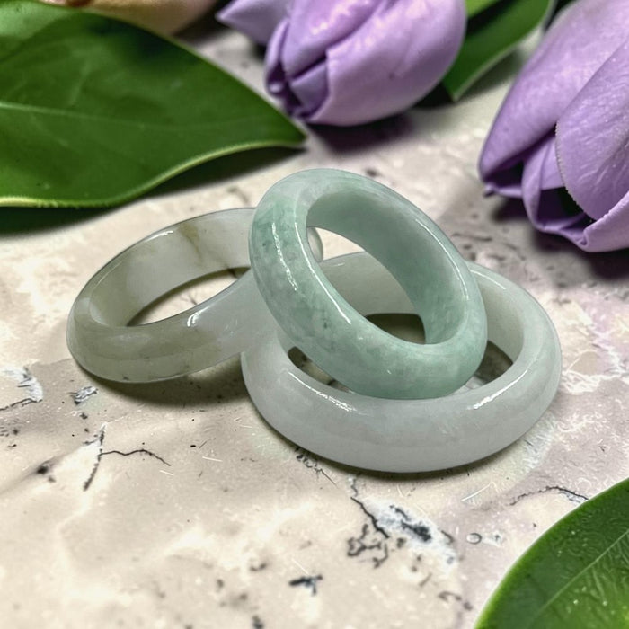 Two light green jade rings with a milky white sheen, displayed on a marble surface with purple tulips in the background.