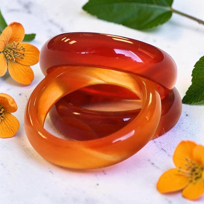 Two Carnelian Rings stacked together on a light marble-like surface, surrounded by small yellow flowers and green leaves.
