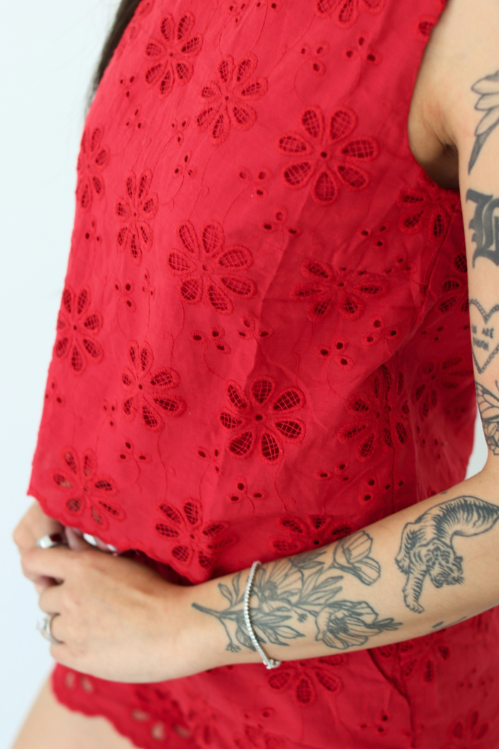 Red lace top with floral patterns worn by a person, showing tattoos on arms.