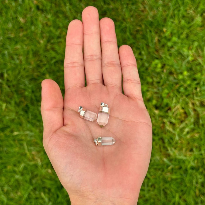 Three small clear crystal point pendants resting on an open palm, with a blurred green grass background.
