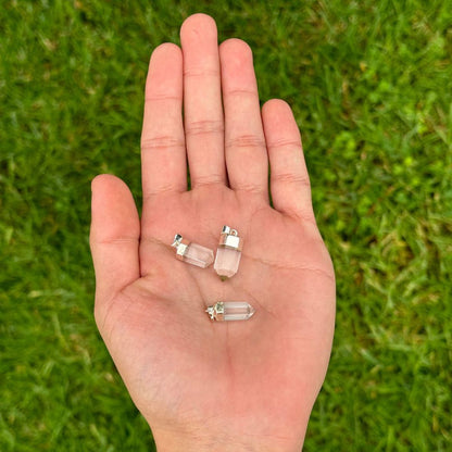Three small clear crystal point pendants resting on an open palm, with a blurred green grass background.