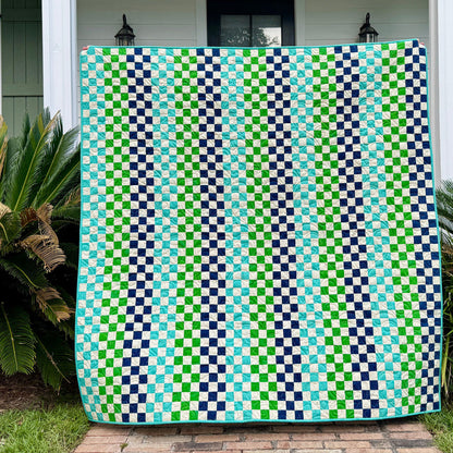 Green and blue patterned quilt draped over a washing machine outside a house.