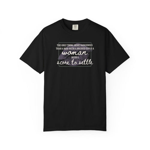 A black Comfort Colors graphic tee from thtgrlreads featuring a bold typographic design saying "The only thing more dangerous than a man with a bruised ego is a woman with a score to settle," part of The Poison Daughter and Tees collections.