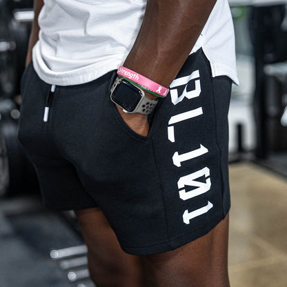 Person wearing black shorts with 'BL101' branding, white shirt, and smartwatch on blurred gym background