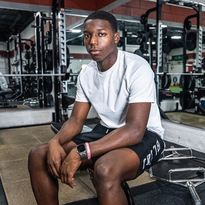 Person sitting on a weight bench in a gym in white BL101 t shirt and black BL101 shorts