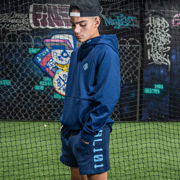Person wearing a blue hoodie and shorts with 'BL101' branding, standing against a graffiti-covered wall.