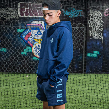 Person wearing a blue hoodie and shorts with 'BL101' branding, standing against a graffiti-covered wall.