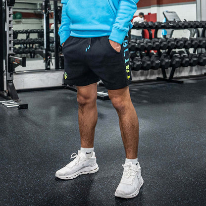 Person wearing a blue sweatshirt, black shorts with BL101 text, and white sneakers in a gym setting.