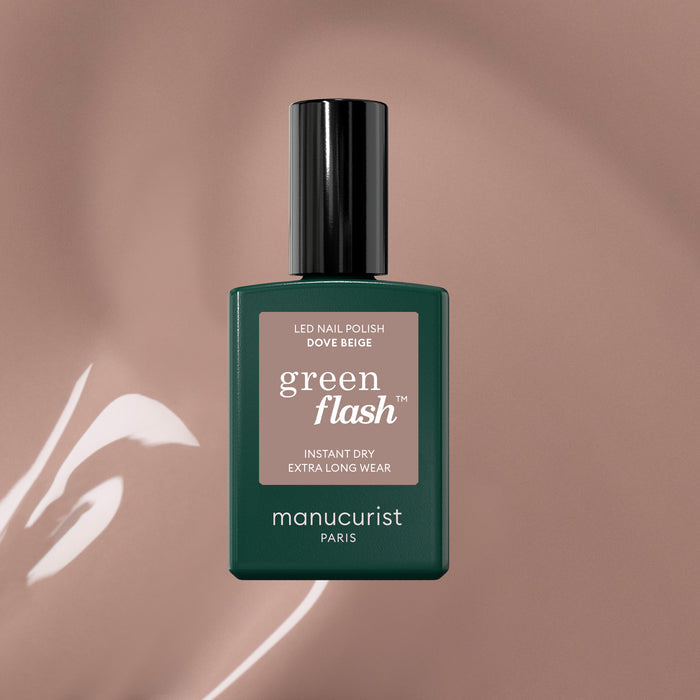 A bottle of Manucurist Dove Beige gel nail polish stands on a glossy taupe surface. Its dark green bottle, black cap, and minimalist label perfectly highlight the pastel beige shade.