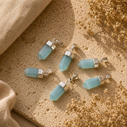Five light blue gemstone pendant charms with silver-toned caps and lobster clasps, arranged on a textured beige stone surface with burlap and dried flowers.