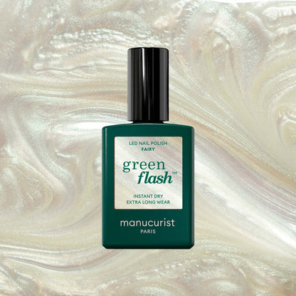 A green bottle of Manucurist Fairy Green Flash LED nail polish with a black cap sits against a shimmery pearl backdrop—ideal for sparkle nails or pairing with pearly white gel polish.
