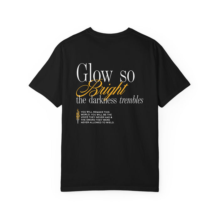 Kindred's Curse Saga Comfort Colors graphic tee from thtgrlreads featuring a vintage washed black fabric with white and gold script text reading "Glow so bright the darkness trembles" from the Glow So Bright | Diem Bellator Tee collection.