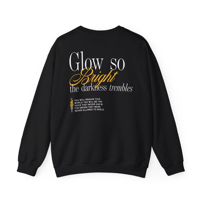 A black Comfort Colors crewneck sweatshirt from thtgrlreads featuring a typographic design with the phrase "Glow so Bright the darkness trembles" in white and orange script fonts on the back.