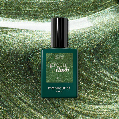 A bottle of Manucurist Groove Green Flash gel polish rests on a swirling, shimmering green background that matches the bold metallic green shade of this striking Manucurist color.