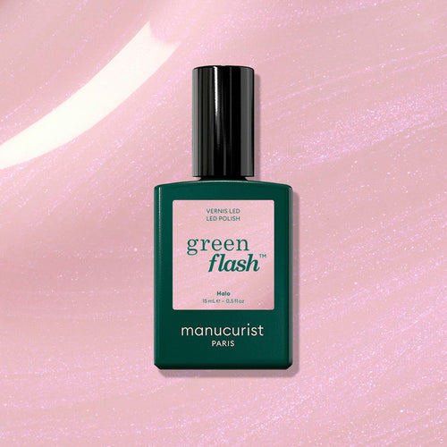 A bottle of Manucurist Halo gel polish stands upright on a shimmery pink background. The dark green bottle with a pale pink label features the product name "Halo" and the Manucurist brand for this innovative LED nail polish.