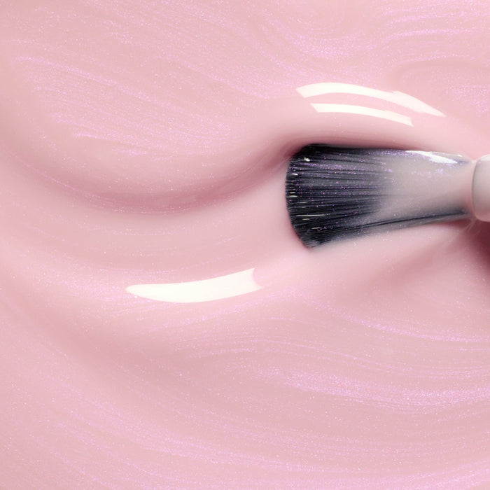 A close-up of a makeup brush swirling through Manucurist's Halo, a glossy light pink gel polish, creating soft wavy textures and shiny highlights.