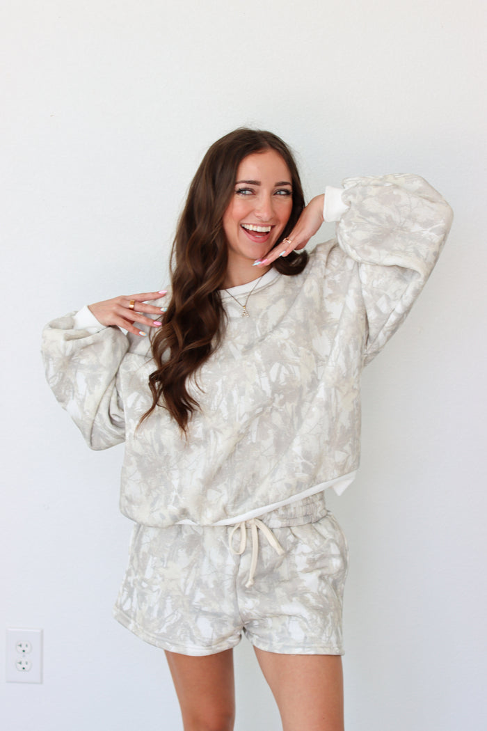 Woman wearing sweatshirt outfit with a camo pattern against a white background