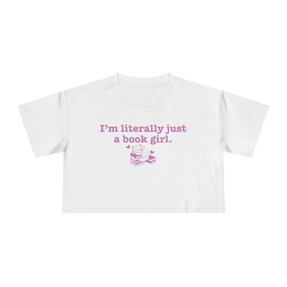 thtgrlreads officially licensed bookish apparel features this Printify white Comfort Colors crop top with vintage wash, soft fabric, and a purple graphic saying "I'm literally just a book girl" above a stack of books illustration, part of the Tees collection.