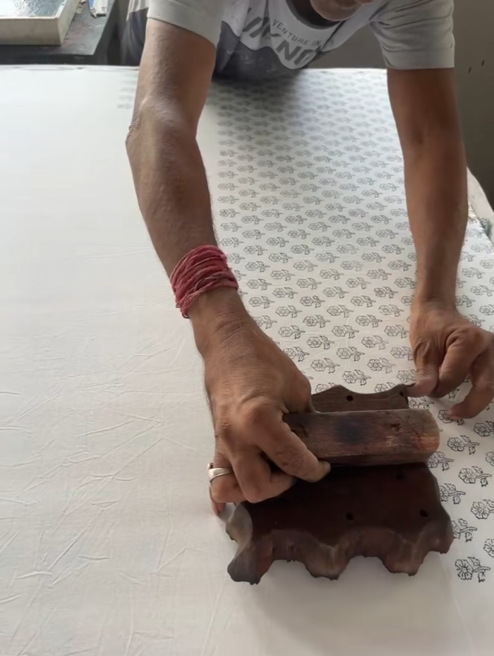 Person using a wooden stamp on a textured surface with a blurred background. Indian Block Prints from Fableism available at globalfibershop.com.