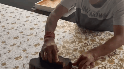 Person using a stamp on a textured surface with a blurred background. Indian Block Prints from Fableism available at globalfibershop.com.