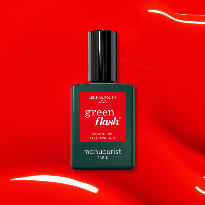 A bottle of Manucurist Lava LED Green Flash nail polish, a pop red gel with warm orange tones, stands on a shiny red surface—ideal for lively summer nights.