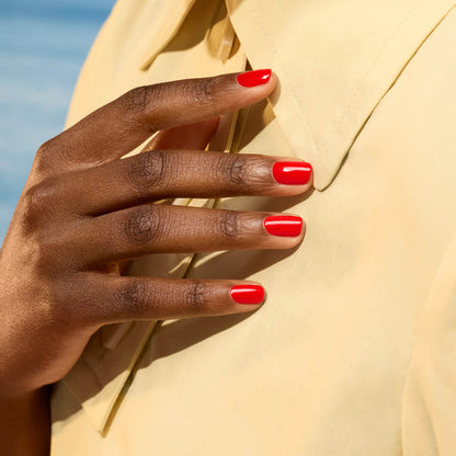 A close-up of a hand with neatly manicured nails painted in Manucurist's Lava Gel Polish rests on the chest of a person wearing a light yellow collared shirt, with a softly blurred background evoking summer nights.
