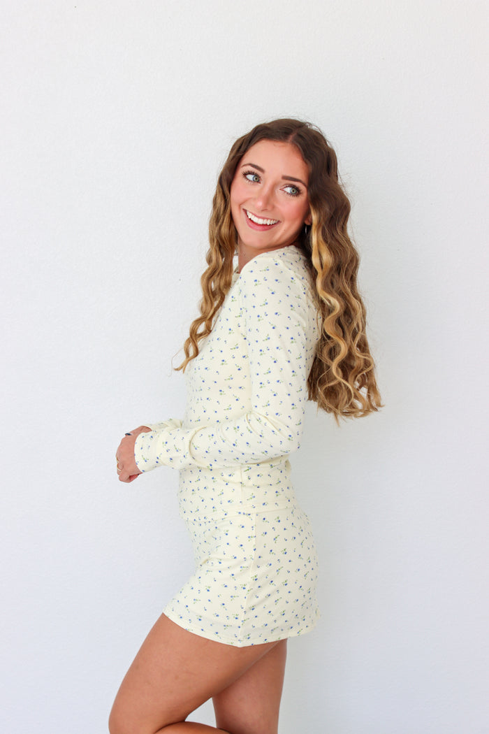 A woman modeling a long-sleeve mini dress with a small, dense all-over print in a light cream or off-white color. The dress has a crew neck and is shown against a plain white studio background.