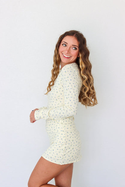A woman modeling a long-sleeve mini dress with a small, dense all-over print in a light cream or off-white color. The dress has a crew neck and is shown against a plain white studio background.