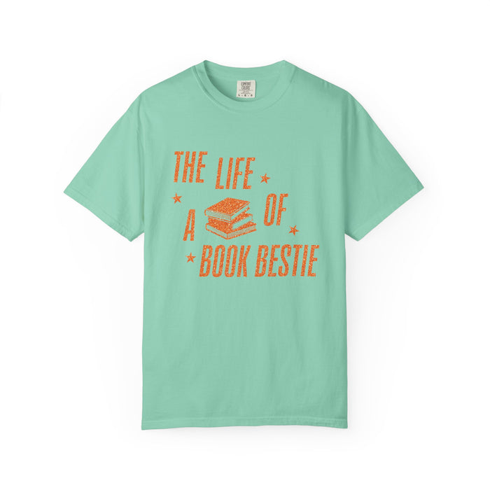 A mint Comfort Colors graphic tee from thtgrlreads featuring a vintage-style orange print of stacked books and the phrase "The Life of a Book Bestie," part of the Book Bestie collection.
