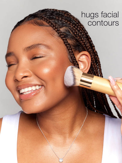 Person applying makeup with a brush to their face, with text 'hugs facial contours' on a gray background.